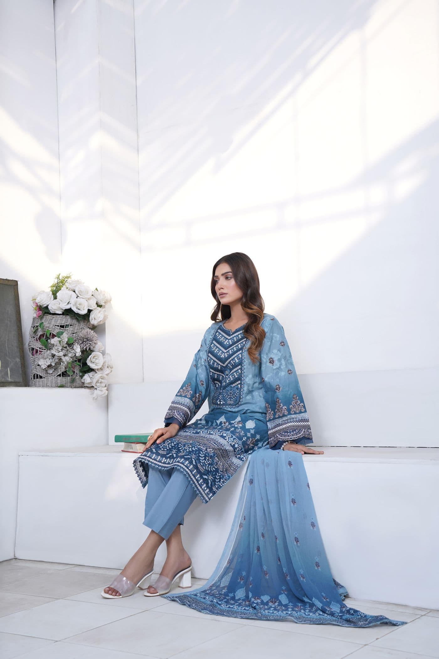 Woman in a blue printed kurta set with a gradient chiffon dupatta seated on a white bench