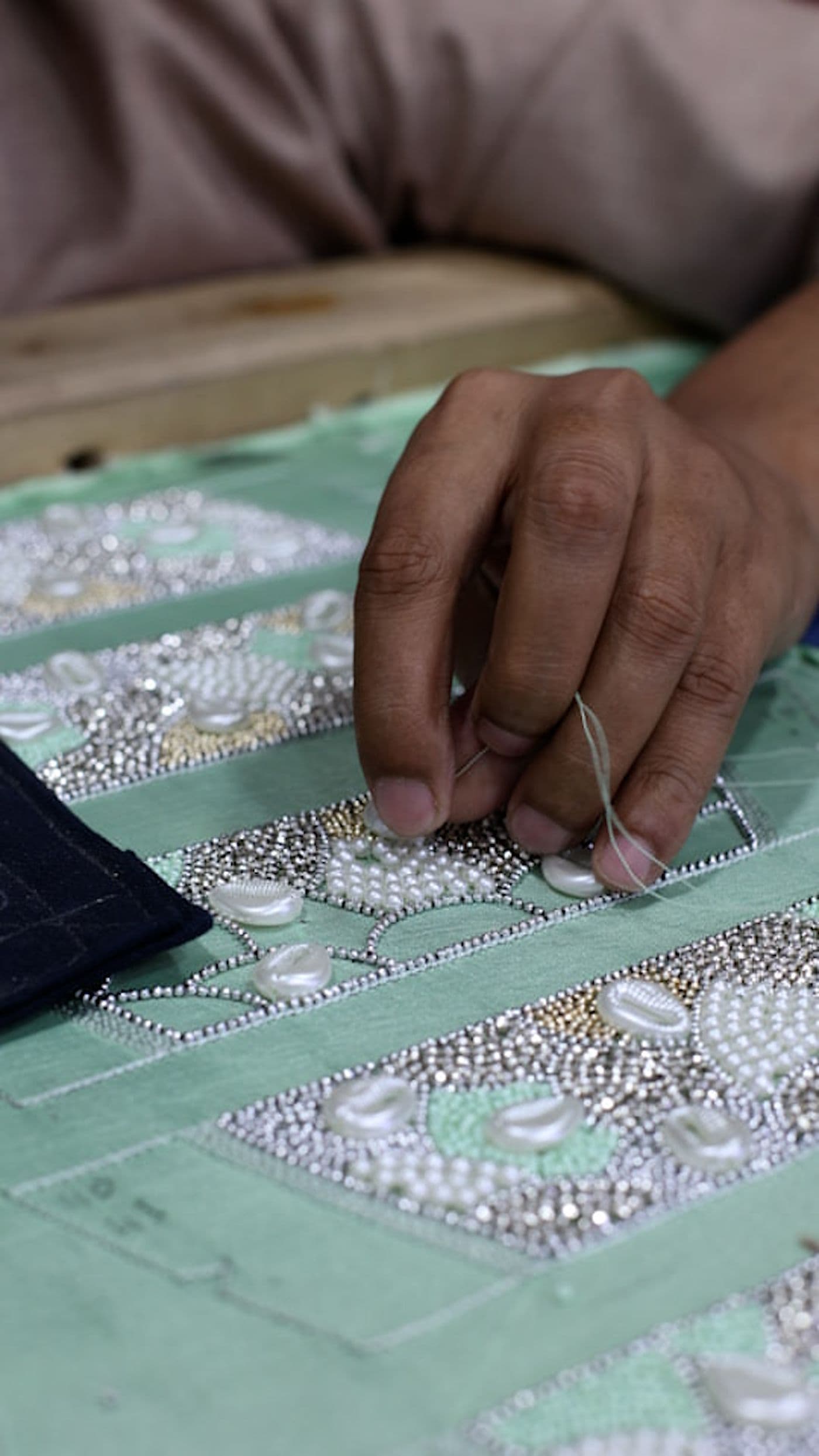 Hands hand-stitching pearls and beads onto green embroidered fabric